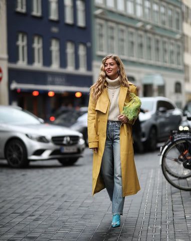 Kvinna i skandinavisk streetstyle med gul trenchcoat och stickad tröja.